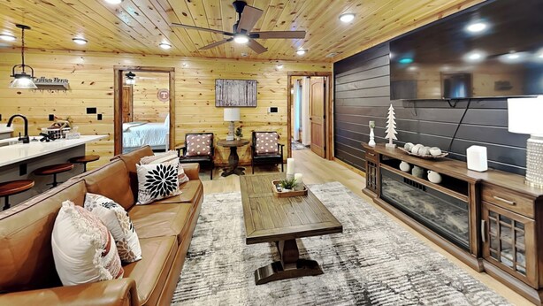 Un intérieur de chalet chaleureux avec un plafond en bois, un canapé, une table basse, une cheminée et un coin repas.