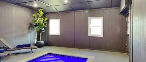 Une salle de spa avec une piscine bleue, un fauteuil de massage et une grande plante en pot.