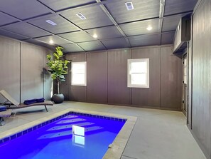 A spa room with a blue pool, a massage chair, and a large potted plant.