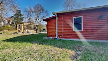 Una cabaña roja de madera con ventana y puerta, un columpio y un patio cubierto de césped.