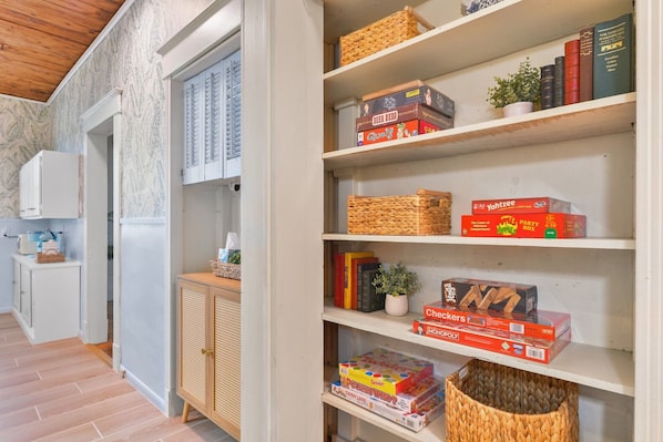 Ein Zimmer mit Holzboden, einem weißen Schrank und Regalen mit Gesellschaftsspielen und Büchern.