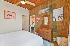 Ein Schlafzimmer mit Bett, Holzk dresser und Spiegel. Eine Tür führt in einen anderen Raum, und eine Wand hat eine bambusartige Struktur.