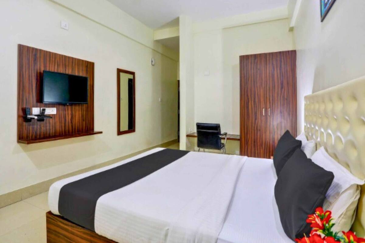 Una habitación de hotel con una cama, un televisor montado en la pared, un escritorio y una silla.