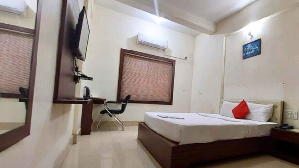 A hotel room with a bed, a desk, a chair, a television, and a window with blinds.