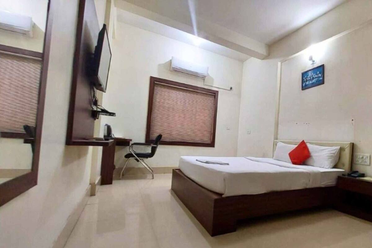 Habitación de hotel con cama, escritorio, silla, televisor y ventana con persianas.