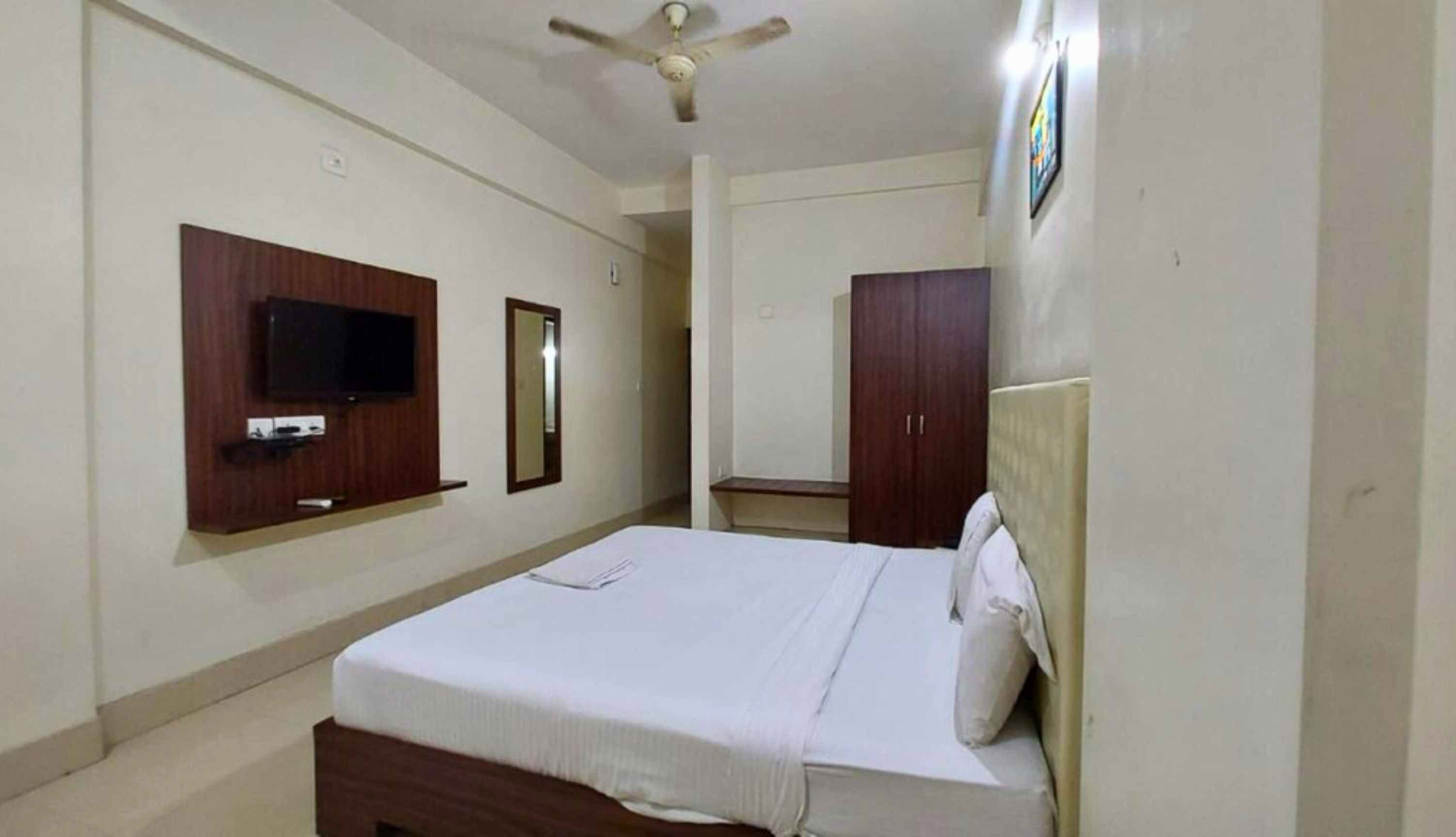 Un dormitorio con cama, televisor montado en la pared, armario y ventilador de techo.