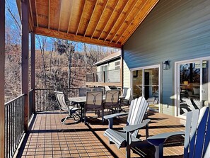 A covered patio with a wooden deck, outdoor furniture, and a view of the surrounding landscape. - The Squirrel's Nest by Jackson Mountain Rentals (Gatlinburg)