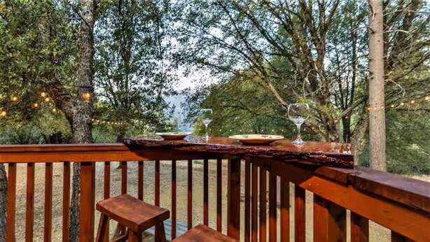 A wooden deck with a table set for two, surrounded by trees and string lights.