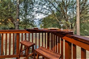 A wooden deck with a table set for two, surrounded by trees and string lights.