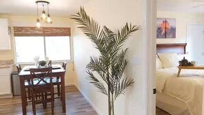A room with a dining area, a large potted plant, and a bed with a headboard.