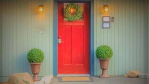 A red door with a wreath, flanked by two potted plants, and a small sign above the door.