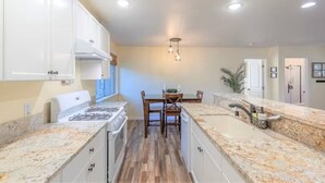 A modern kitchen with white cabinets, a gas stove, wooden flooring, and a dining area with a table and chairs.