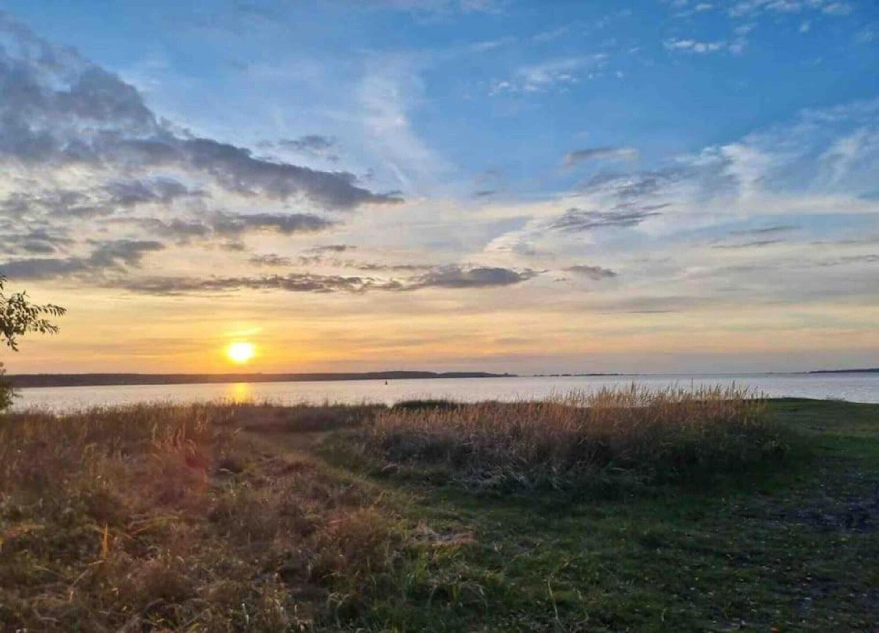 A sunset over a body of water with grassy areas in the foreground.