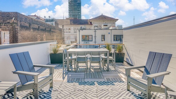 Eine Dachterrasse mit Tisch und Stühlen, einem gemusterten Teppich und Blick auf Gebäude im Hintergrund.