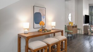 Ein modernes Wohnzimmer mit Couchtisch aus Holz, zwei Stühlen, einem Fernseher und einer Essecke mit Holztisch und Stühlen.