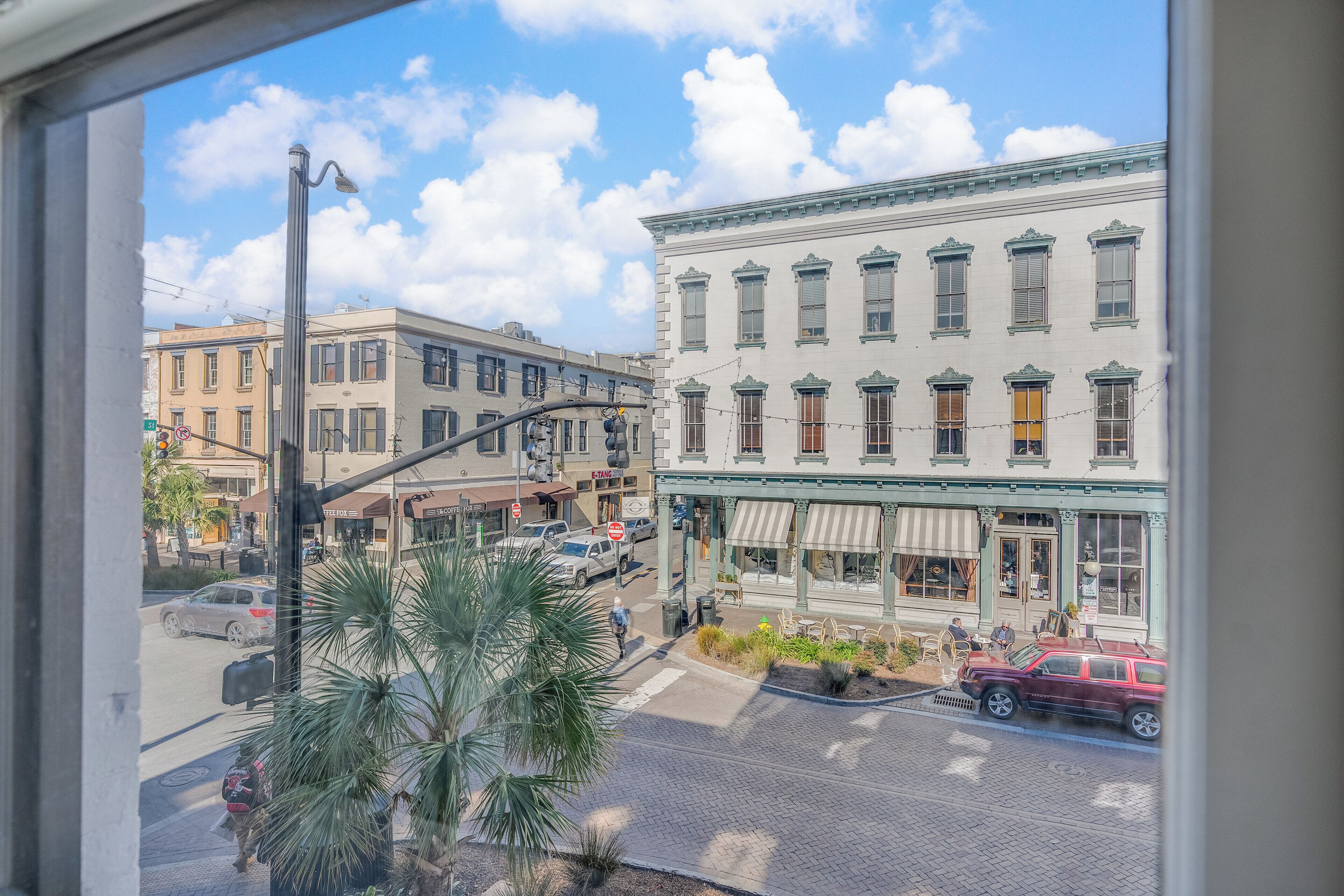 A street view with buildings, a palm tree, and parked cars.