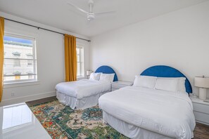 Una habitación de hotel con dos camas, un ventilador de techo, una ventana con cortinas y una alfombra estampada.