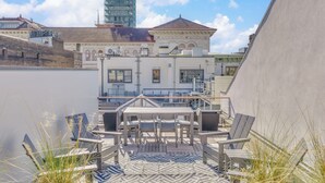 Terraço no telhado com mesa e cadeiras, vista para paisagem urbana com edifícios históricos e um arranha-céu moderno.