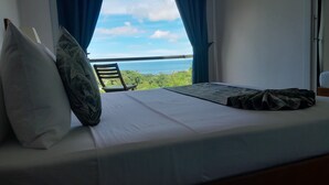 En säng med utsikt över havet, en stol och ett fönster med blå gardiner.