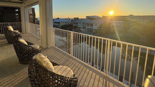 Een balkon met rieten meubels en uitzicht op de ondergaande zon boven het water.