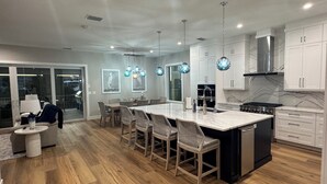Een moderne keuken met witte kasten, een groot eiland en hanglampen.