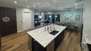 Een moderne keuken met een marmeren eiland, zwarte kastjes en hanglampen.