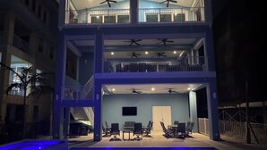 Een modern gebouw met twee verdiepingen, een dakterras, een buiten zitgedeelte en een zwembad met blauwe verlichting.