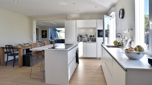 Une cuisine moderne avec des meubles blancs, un îlot central et un coin repas comprenant des chaises et une table.