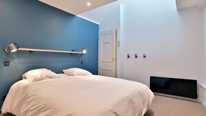 Une chambre à coucher avec un lit, une lampe de chevet, une porte et un téléviseur fixé au mur.