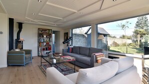 Un salon moderne avec un canapé, une table basse et une bibliothèque. Une grande fenêtre offre une vue sur l’extérieur.