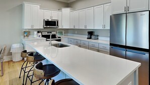 A modern kitchen with white cabinets, stainless steel appliances, and a central island with bar stools. - Coastal Grove by Southern Vacation Rentals (Santa Rosa Beach)