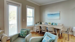 A spacious dining area with a high table and multiple chairs, a seating area with two sofas, and large windows with blinds. - Coastal Grove by Southern Vacation Rentals (Santa Rosa Beach)