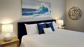 A hotel room with a large bed, two bedside tables with lamps, a wall-mounted artwork of a wave, and a decorative wall piece. - Coastal Grove by Southern Vacation Rentals (Santa Rosa Beach)