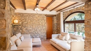 A stone-walled room with a wooden ceiling, a large arched window, and a white sofa set. - Majordoms Molí - La Garrotxa (Beuda)