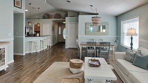 A spacious living room with a dining area, kitchen, and a ceiling fan. - Emerald Port Of Call by Southern Vacation Rentals (Miramar Beach)