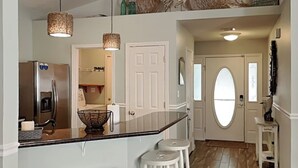 A kitchen with a central island, two bar stools, a refrigerator, and hanging pendant lights. - Emerald Port Of Call by Southern Vacation Rentals (Miramar Beach)