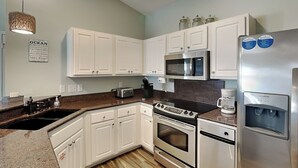 A modern kitchen with white cabinets, stainless steel appliances, a granite countertop, and a wooden floor. - Emerald Port Of Call by Southern Vacation Rentals (Miramar Beach)