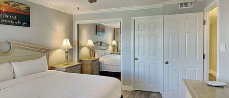 A hotel room with a bed, bedside lamps, a ceiling fan, a mirror, and a door.