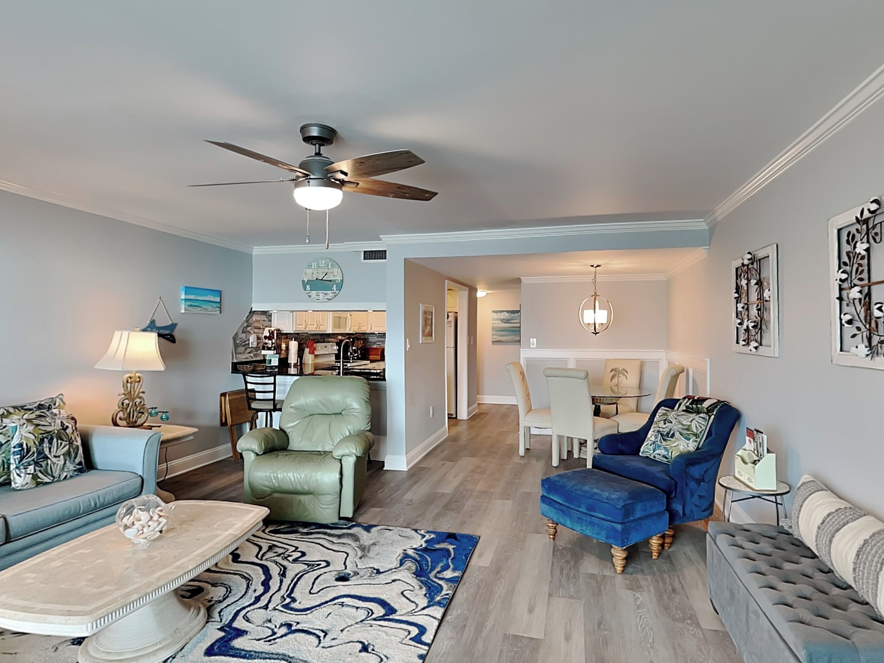 A spacious living room with a ceiling fan, a dining area, and a kitchen in the background.