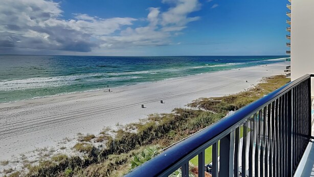 A beach view from a balcony with a railing, ocean, and clear sky.
