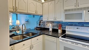 A kitchen with white cabinets, a black countertop, a stainless steel sink, a microwave, and an oven.