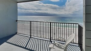 A balcony with a view of the ocean, a white chair, and a black railing.