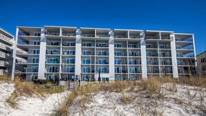 A multi-story hotel with balconies, located near a sandy beach area.