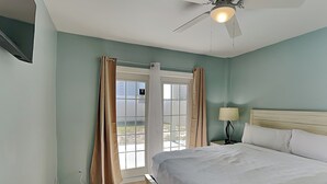 A bedroom with a bed, a ceiling fan, a nightstand with a lamp, and a view through a door. - PC Beach Retreat B by Resort Collection (Panama City Beach)