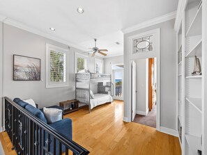 Un salón espacioso con piso de madera, un sofá blanco, una cuna para bebé y un ventilador de techo.