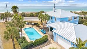 Une maison à deux étages avec une piscine, entourée de palmiers et offrant une vue sur l’océan.