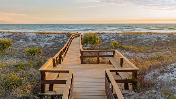 Une promenade en bois menant à la plage, avec des bancs et une vue dégagée sur l’océan.
