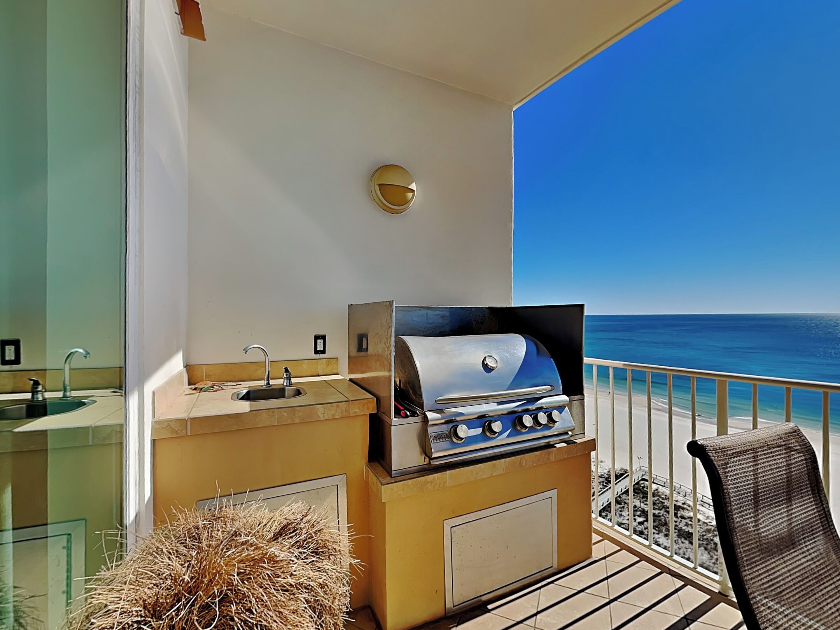 A balcony with a grill, a sink, and a chair.