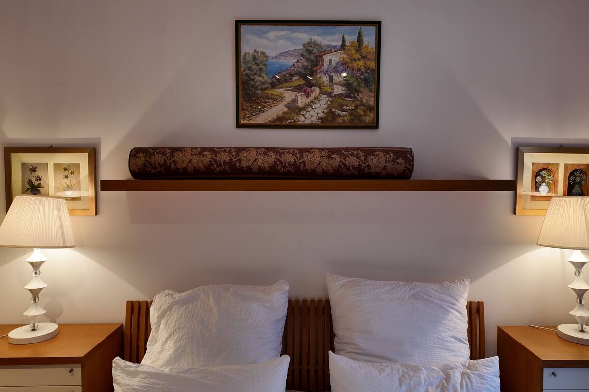 Habitación de hotel con dos camas, un cuadro en la pared y dos mesitas de noche con lámparas.