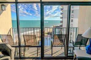 A balcony with a view of the beach and ocean, a chair, a table, and a lamp. - Sand Dunes 1246 (Myrtle Beach)